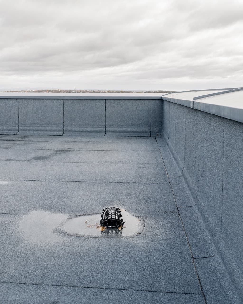 Une toiture terrasse en membrane bitumineuse grise avec un relevé en acrotère et une naissance d’évacuation