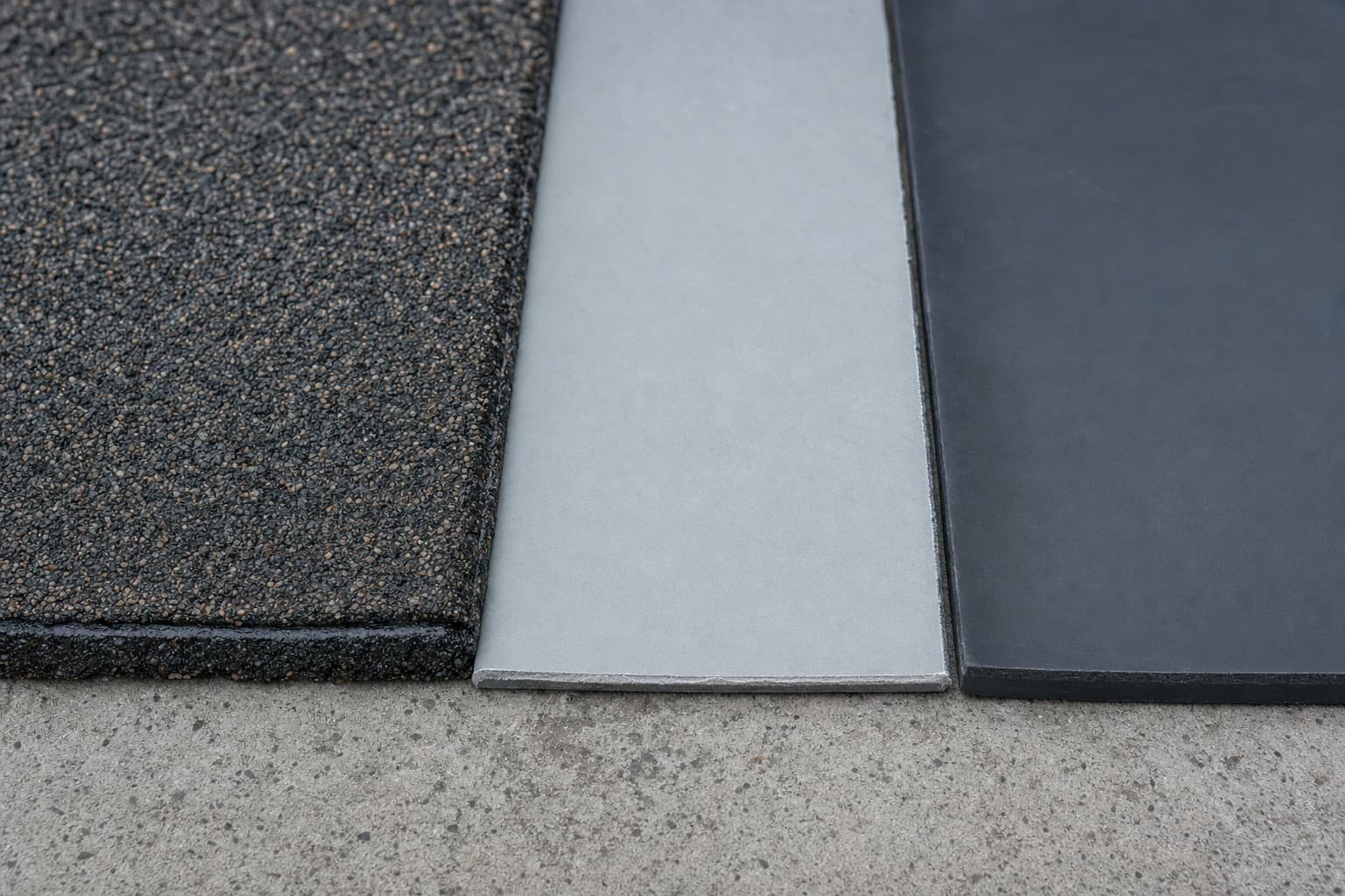 Trois échantillons de membrane côte à côte : bitume granulé, monocouche gris clair, élastomère sombre