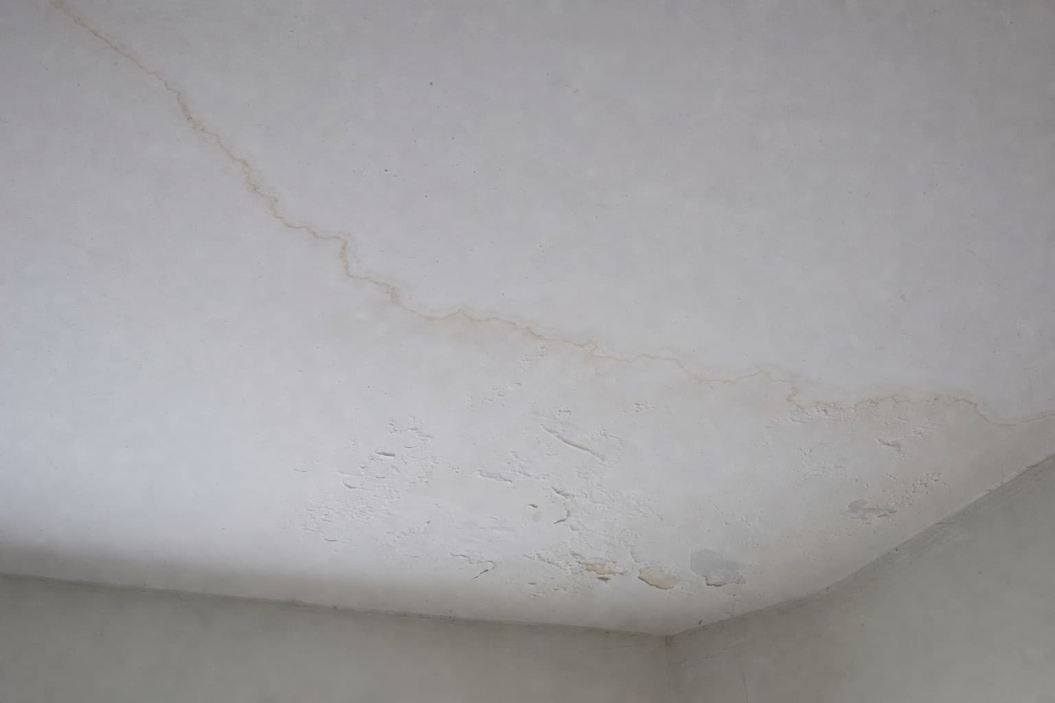 Une tache d’eau qui s’étend sur un plafond intérieur, l’enduit cloqué au bord